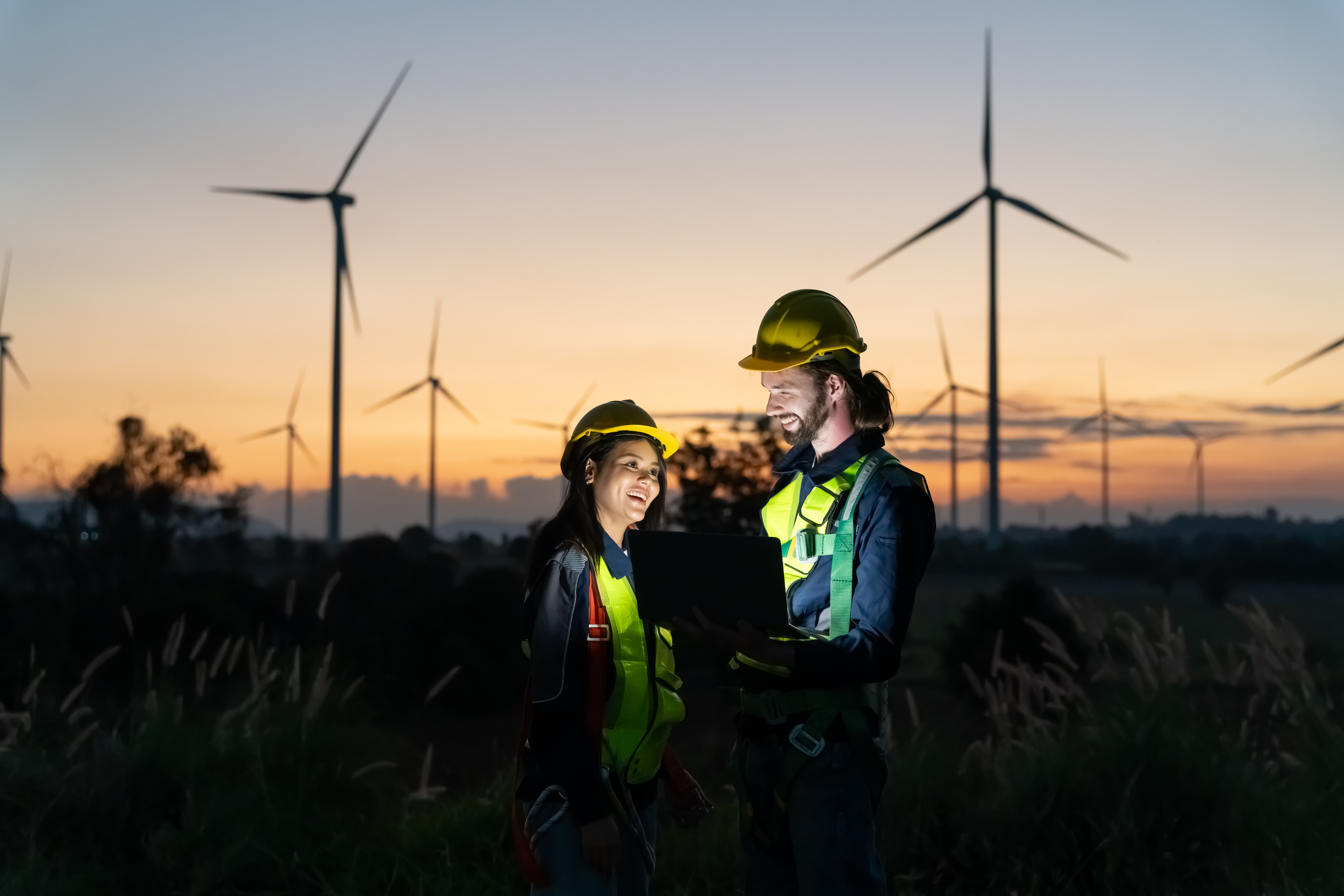 Multiracial colleagues examining wind turbines blueprints. Windmills on sunset